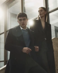 Two models posing indoors by a large window with warm sunlight filtering through for Manuel Ritz FW26 collection.