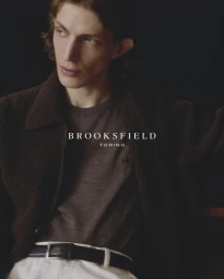 Close portrait of a male model wearing a dark brown knitted cardigan against a dark background for Brooksfield FW26.