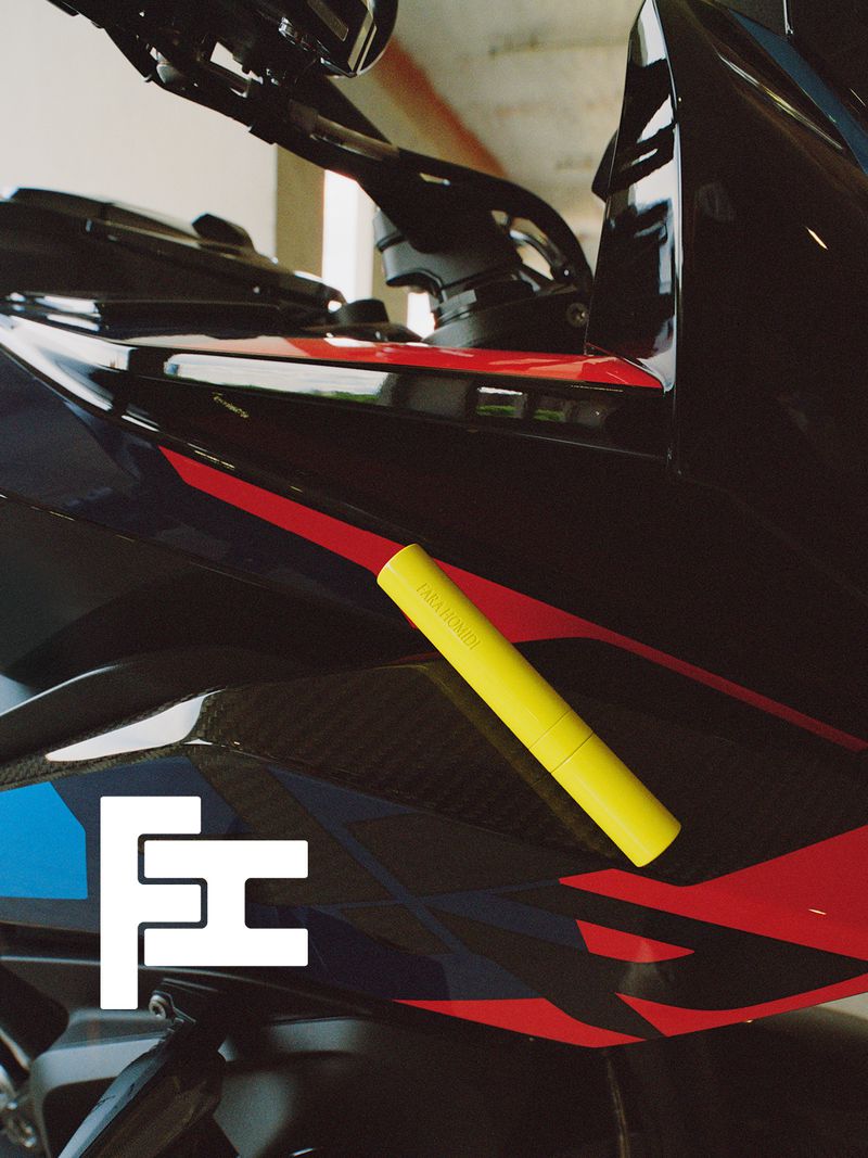 Bright yellow cosmetic tube placed against the black, red, and blue bodywork of a motorcycle