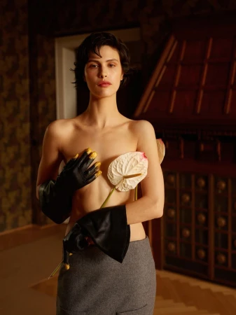 Model with dark hair wearing black leather gloves and holding white anthurium flowers for an editorial shoot.