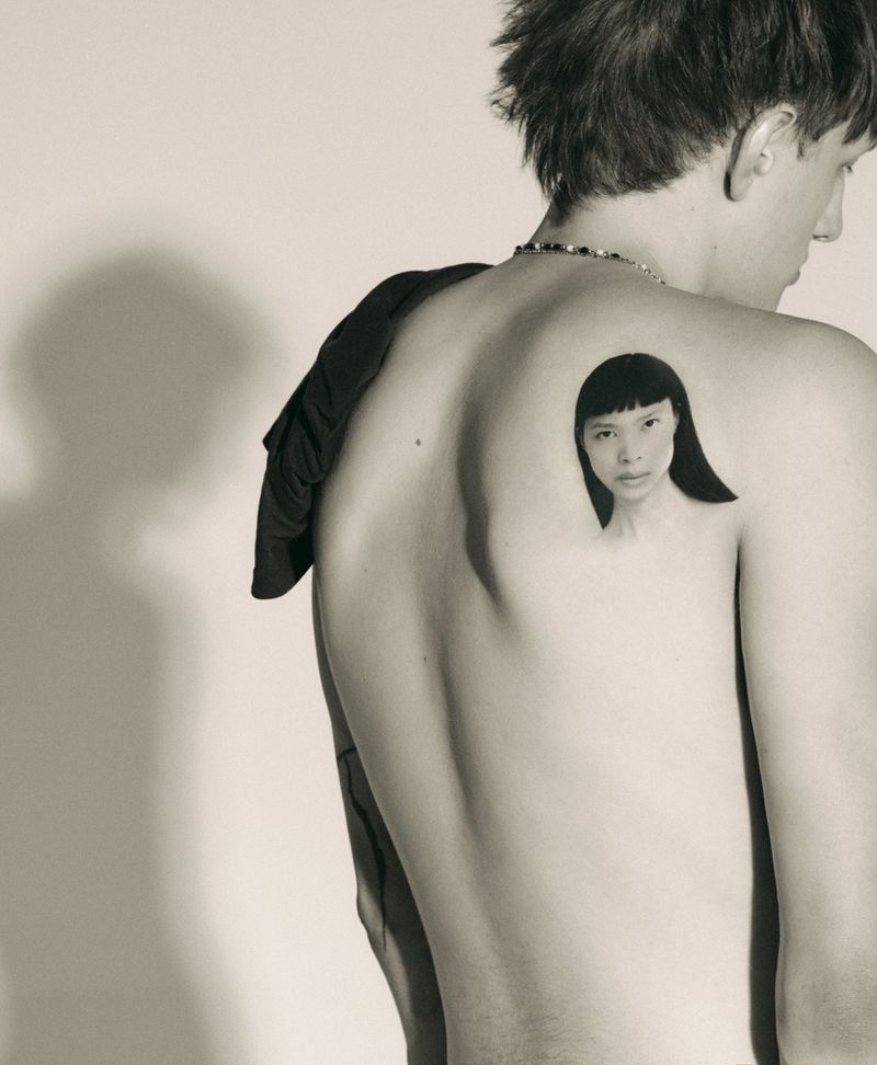 Close-up portrait of a model with short dark hair and a portrait tattoo on their back, photographed by Arseny Jabiev.