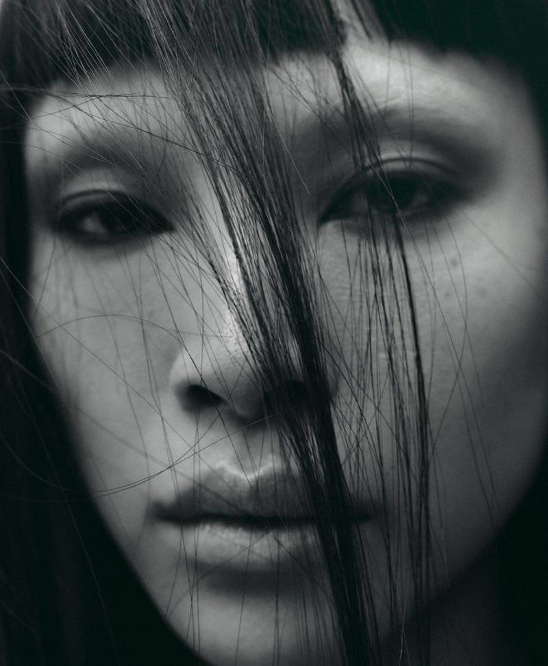 Extreme close-up portrait of model Diane Chiu with dark hair strands falling across her face in a moody black and white aesthetic.