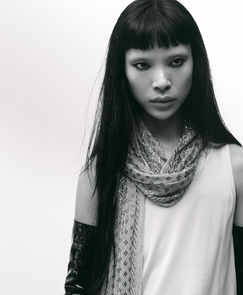 Model Diane Chiu in a white tank top and patterned scarf with black gloves against a white background