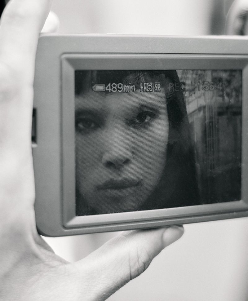 Close-up of a person holding a digital camera displaying a black and white portrait of model Diane Chiu on screen.