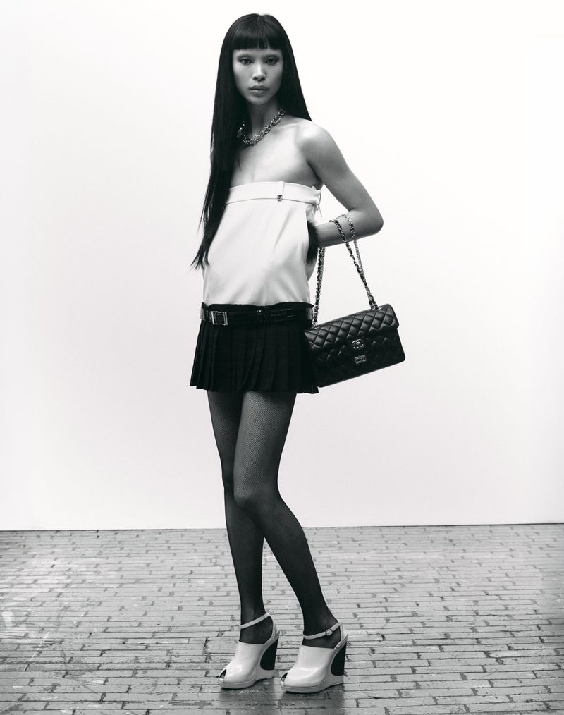 Model Diane Chiu in a white top and black skirt holding a quilted handbag against a plain background