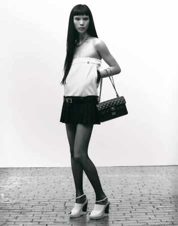 Model Diane Chiu in a white top and black skirt holding a quilted handbag against a plain background