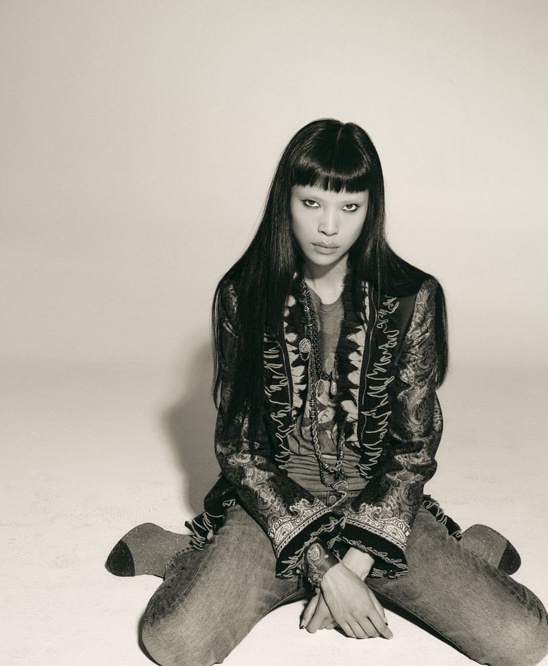Model Diane Chiu kneeling against a plain light background wearing patterned jacket and jeans
