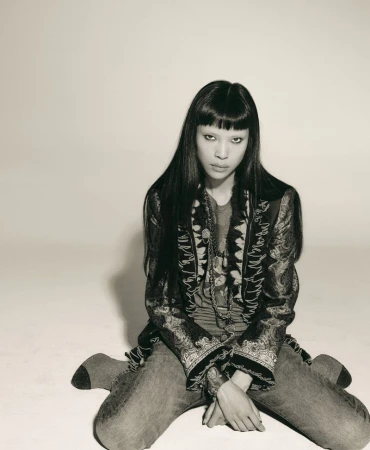 Model Diane Chiu kneeling against a plain light background wearing patterned jacket and jeans