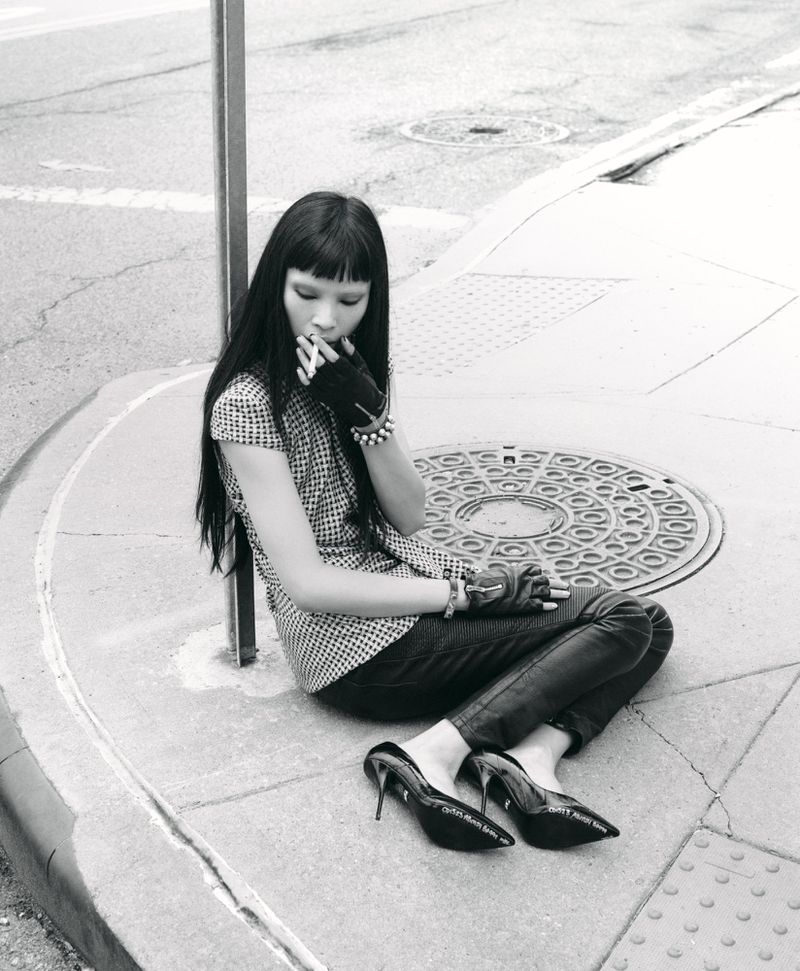 Model Diane Chiu sits on a concrete sidewalk smoking next to a metal pole for Rouge Fashionbook, photographed by Arseny Jabiev.