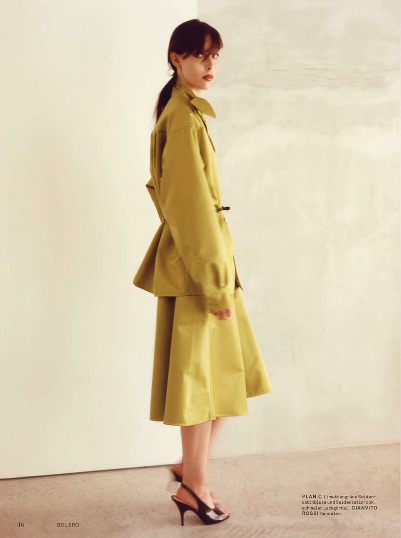 Model in olive green blouse and skirt standing against a pale wall for Bolero Magazine Back to the Future editorial