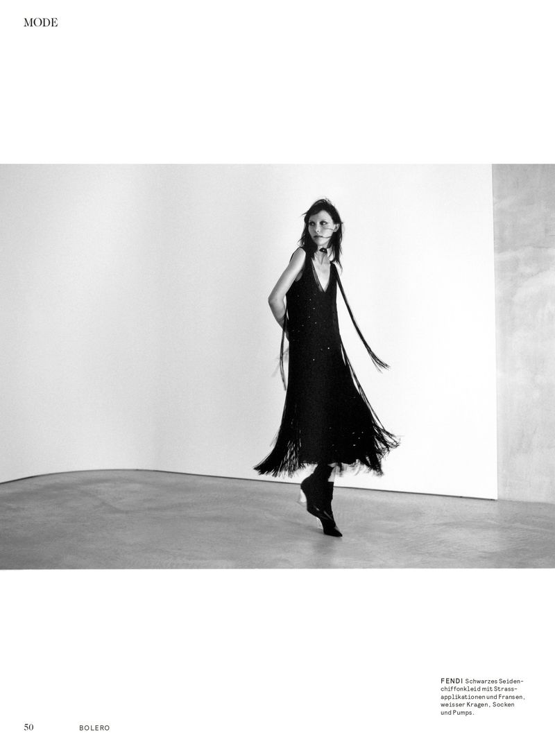 Model in black fringe dress walking across a concrete floor in a minimalist white studio space