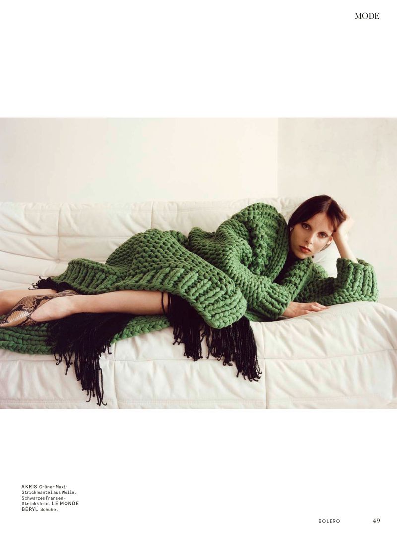Model lying on a white tufted sofa wearing a chunky green knit cardigan and fringe dress for Bolero Magazine.