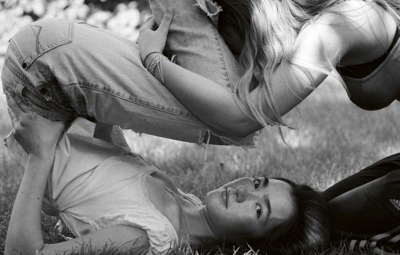 Two women posing together on grass in a black and white monochrome photograph by photographer Mel Bles.