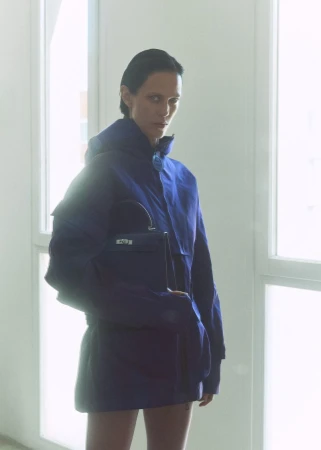 Model Aymeline Valade wearing a blue jacket and holding a handbag in front of bright windows for M Le magazine du Monde
