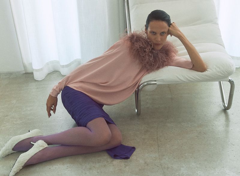 Model Aymeline Valade in a pink feather-trimmed top leaning against a white leather lounge chair in M Le magazine du Monde editorial.