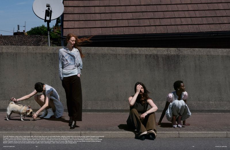 Four models outdoors against a concrete wall and pavement, featuring a standing red-haired woman and a small dog on a leash.