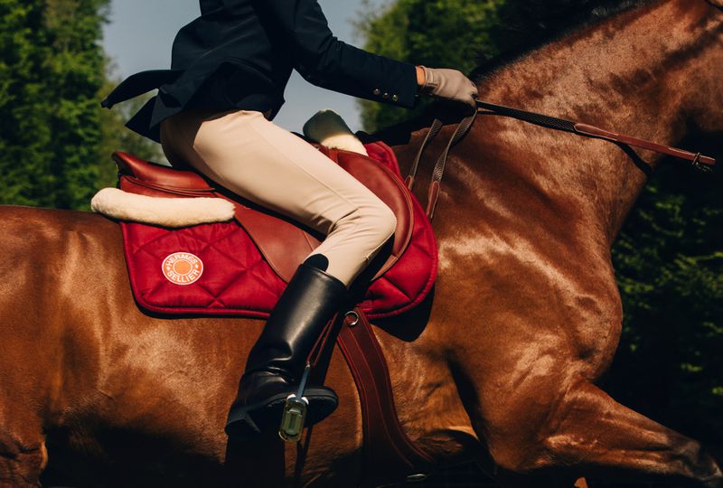 Close-up of a person riding a brown horse wearing a dark blazer beige trousers and black riding boots