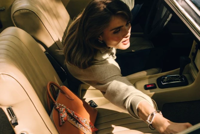 Woman in beige sweater seated in a leather car interior with a tan handbag
