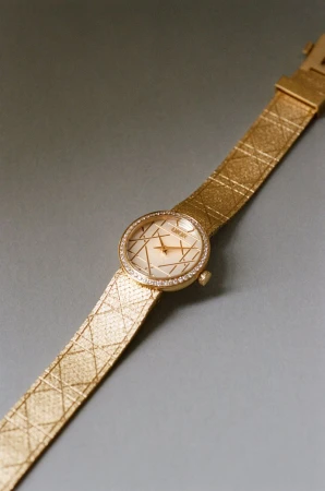 Gold luxury wristwatch with diamond bezel and textured strap resting on plain grey surface