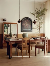 Interior shot of a dining room with a long wooden table, matching wooden chairs, pendant lights, and a framed floral painting on the wall.