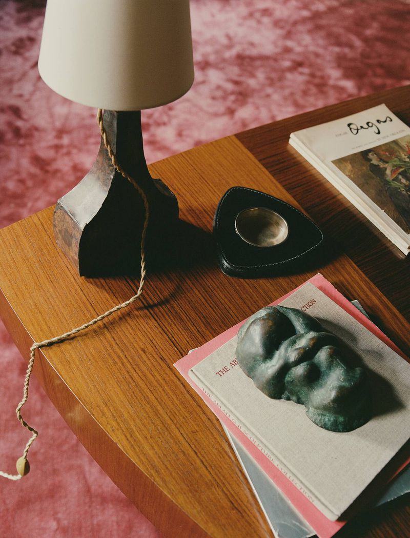 Close-up interior shot of a wooden coffee table styled with books, a lamp, and a small sculpture by photographer Clément Pascal.