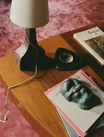 Close-up interior shot of a wooden coffee table styled with books, a lamp, and a small sculpture by photographer Clément Pascal.