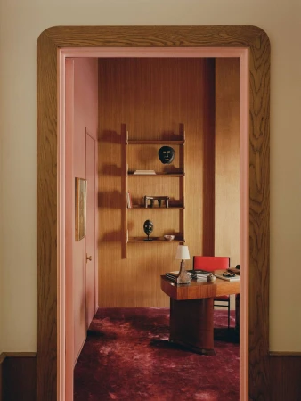 Interior view through a rounded wooden doorway into a home office with wood paneling, a desk, shelving, and a patterned rug.
