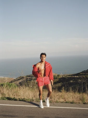 Man wearing red jacket and shorts walking along a coastal road with the ocean in the background