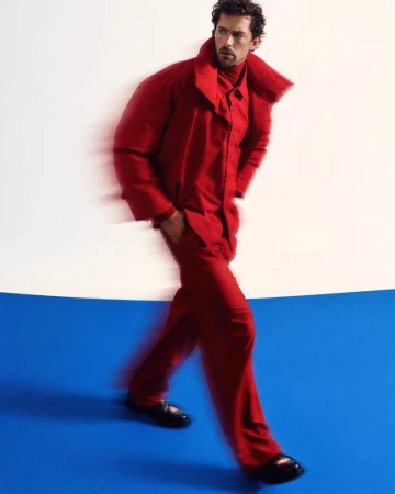 Model Christian Hogue wearing a red coat and trousers walking against a studio backdrop for TMRW Magazine editorial
