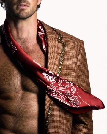 Close-up of male model Christian Hogue wearing a patterned red scarf and brown houndstooth jacket against white.