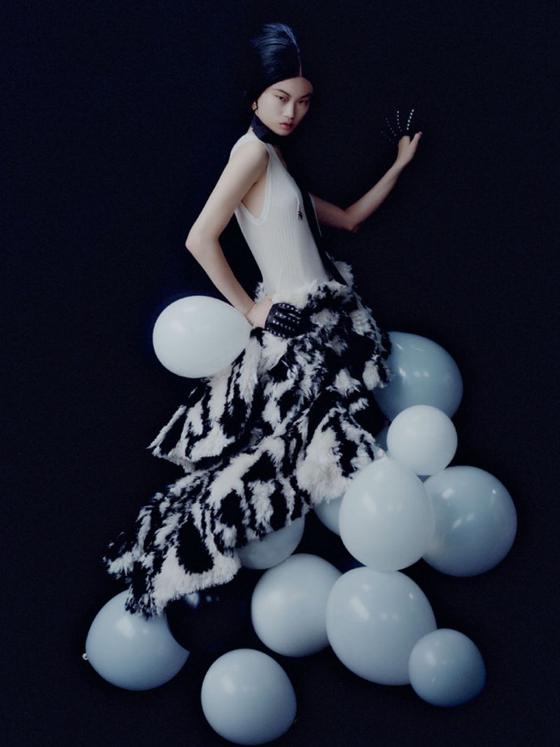 Model in white top and black-and-white skirt surrounded by white balloons against a dark background for Mixte