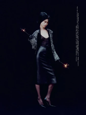 Model wearing a patterned jacket and black leather skirt holding sparklers against a black background.