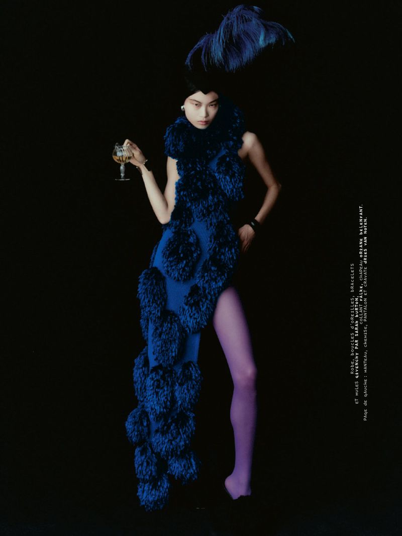 Model in blue feathered dress holding a glass against a dark background for Mixte editorial