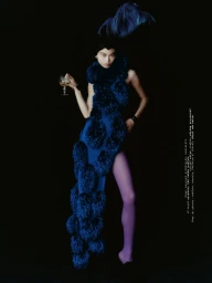 Model in blue feathered dress holding a glass against a dark background for Mixte editorial