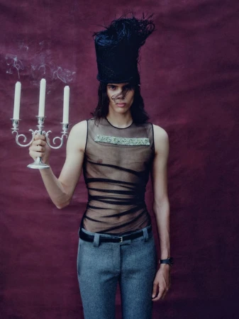 Model wearing a tall black hat and sheer black top holding a silver candelabra against a deep burgundy backdrop for Mixte.