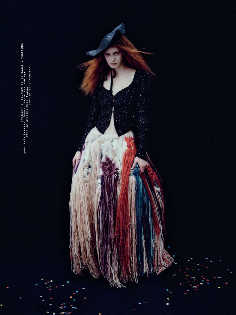 Model with red hair wearing a black cardigan and textured fringed skirt against black