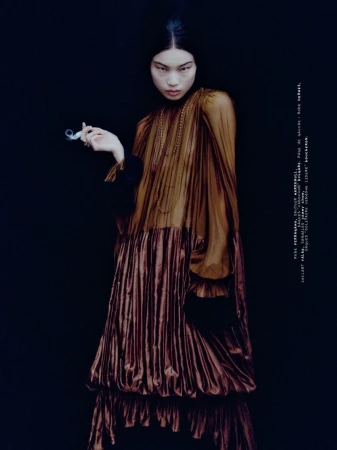 Model Elizabeth Nepola wearing a pleated brown dress and long necklaces in The Secret Party project for Mixte, shot by Julius Bohlin.