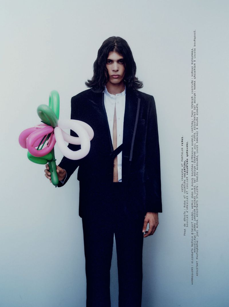 Model with long dark hair wearing a black blazer and white shirt holding a bouquet of colorful balloon animals.