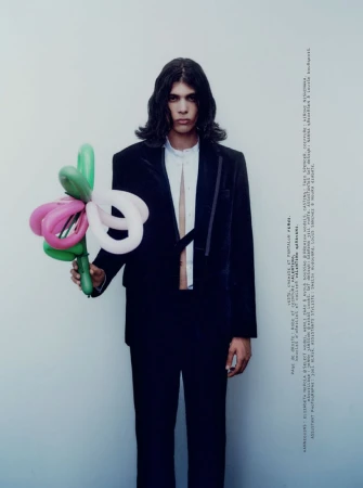 Model with long dark hair wearing a black blazer and white shirt holding a bouquet of colorful balloon animals.