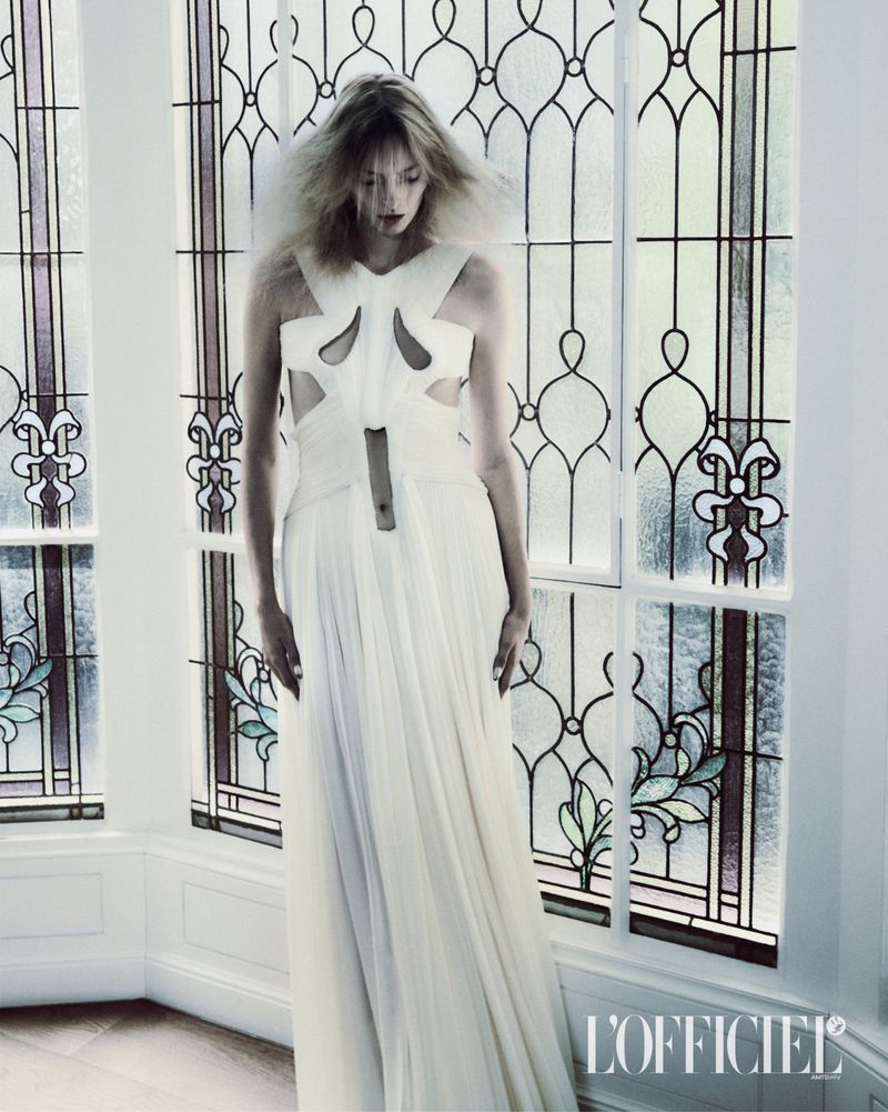 Model Elza Matiz in a white cutout dress standing before large stained glass windows for L'Officiel Italia.