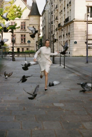 Model running along a European city street surrounded by fluttering pigeons