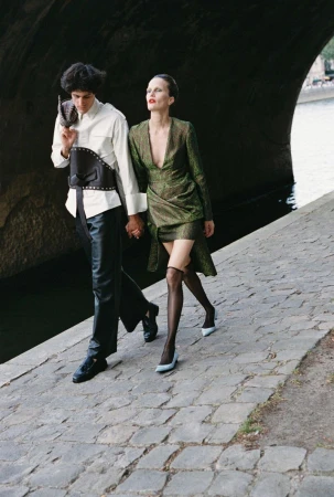 Two models walking together along a stone riverbank under a large bridge for Harper's Bazaar Kazakhstan