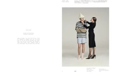 Two models posing in a studio with a grey seamless background, featuring a woman in a black dress touching a man wearing a paper hat.
