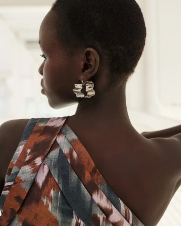 Close-up profile of a Black woman with short hair wearing a wavy silver earring and a patterned one-shoulder garment.
