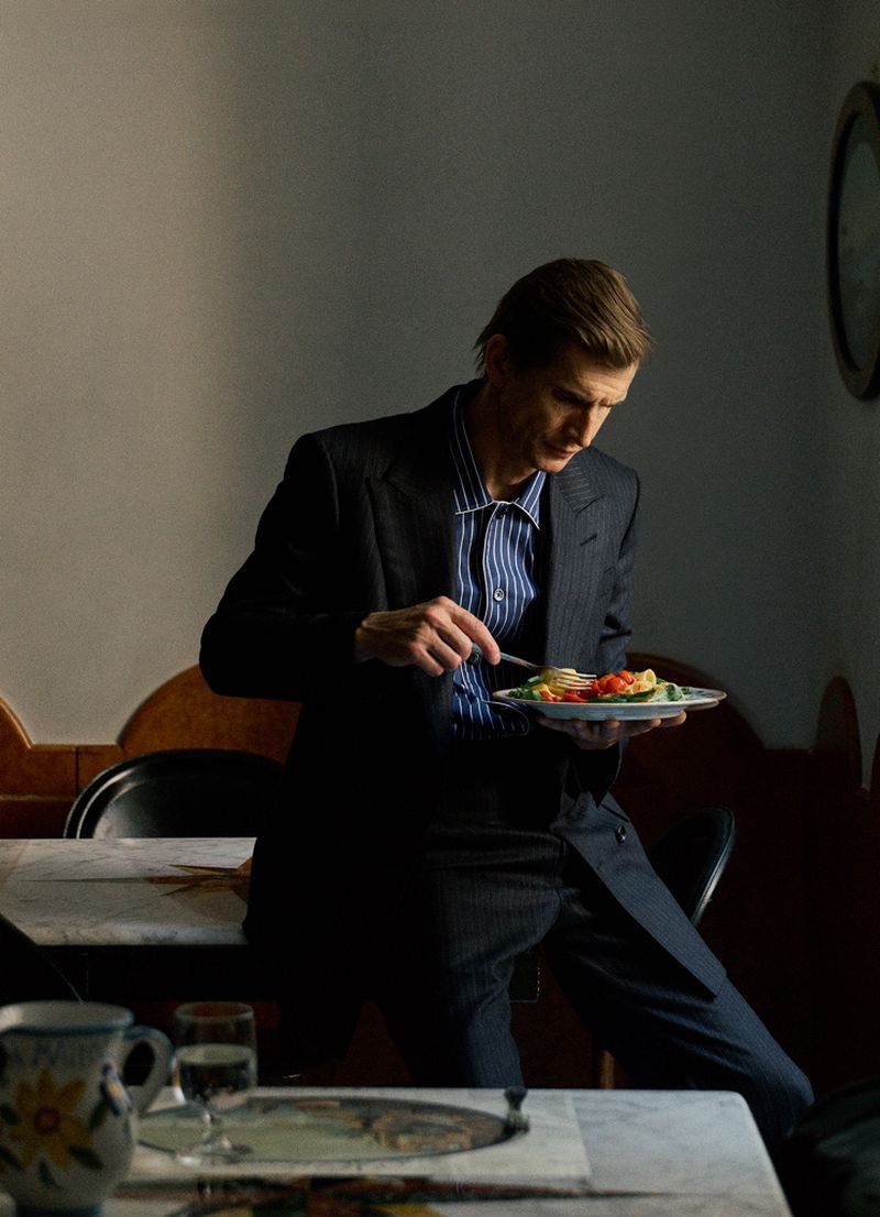 A man in a pinstriped suit jacket eating a salad plate in an indoor setting photographed by Raffo Marone