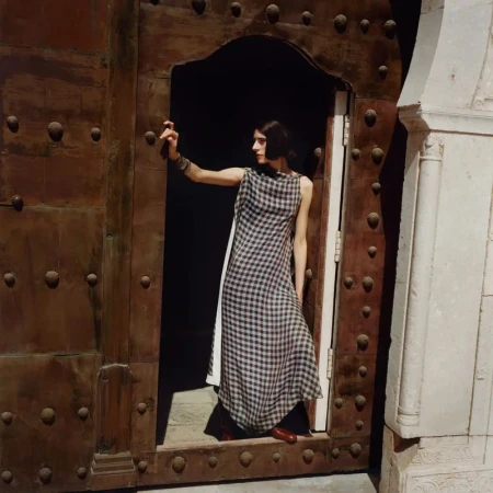 Model wearing a patterned dress standing in a tall wooden doorway with decorative studs