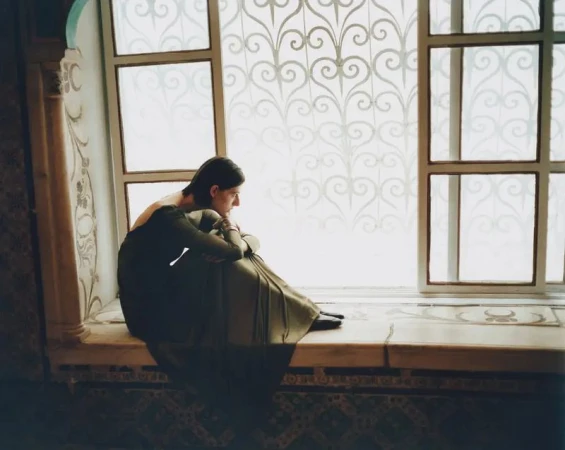 Model seated on a wide tiled windowsill indoors against an ornate frosted glass window for Sotheby's