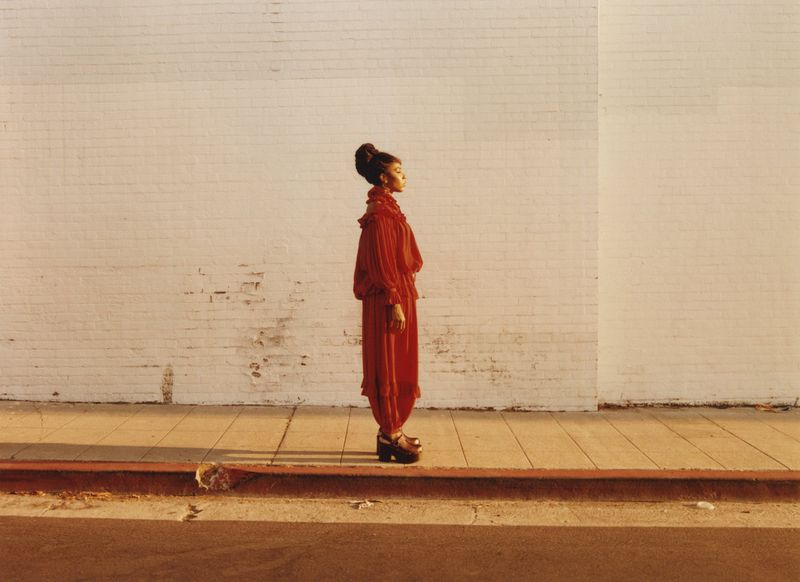 Woman in a red ruffled dress standing in profile against a light brick wall during golden hour sunlight.