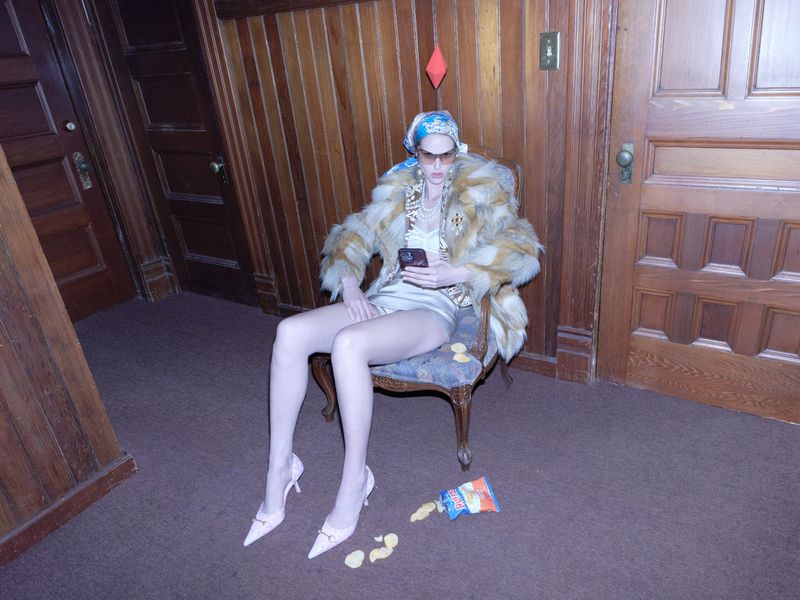 Model Abby Champion wearing fur coat and headscarf seated in wood-paneled room for Rouge Fashionbook