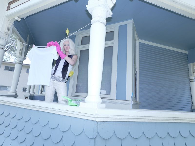 Blonde model hanging a white t-shirt on a clothesline on a blue porch for Rouge Fashionbook